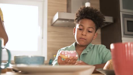 young boy happily eating a delicious pink donut
