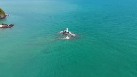 drone footage captures a lighthouse on a rocky outcrop in the andaman sea, surrounded by turquoise waters near phuket, thailand
