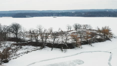 Aerial-shot-of-empty-winter-forest-on-the-shores-of-a-frozen-snow-covered-lake