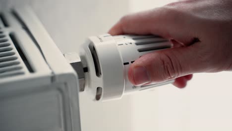 primer plano de la mano masculina subiendo el calor en un radiador de calefacción aumentando el ajuste de la temperatura