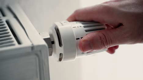 close up of male hand turning up the warmth on a heater radiator increasing adjusting the temperature