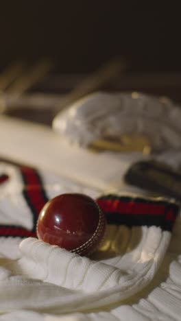 Cricket-Stillleben-Mit-Nahaufnahme-Einer-Hand,-Die-Den-Ball-Fallen-Lässt,-Mit-Schlägerhandschuhen,-Stümpfen,-Pullover-Und-Kautionen-Im-Hintergrund