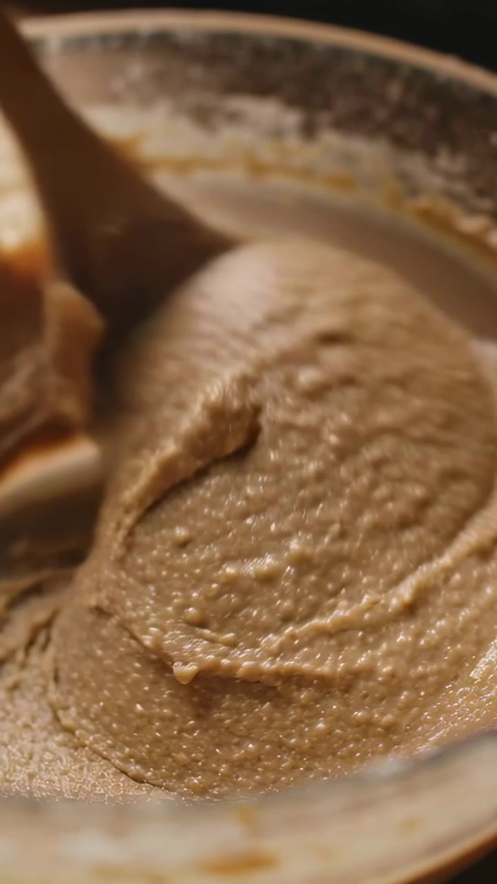 Vertical video: Pressing spoon at rim of glass bowl, scooping and smoothing thick batter on counter