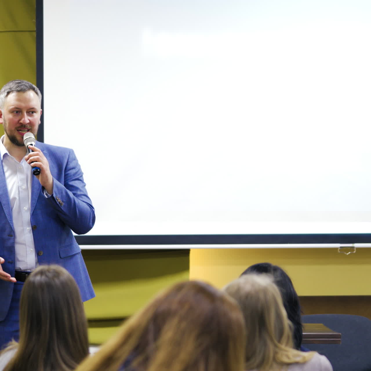 Businessman in white shirt and blue suit explaining new program to the audience. Handsome man conducts a lecture gesuring a lot in a conference hall.