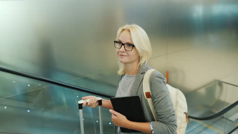 woman on escalator with tablet and suitcase