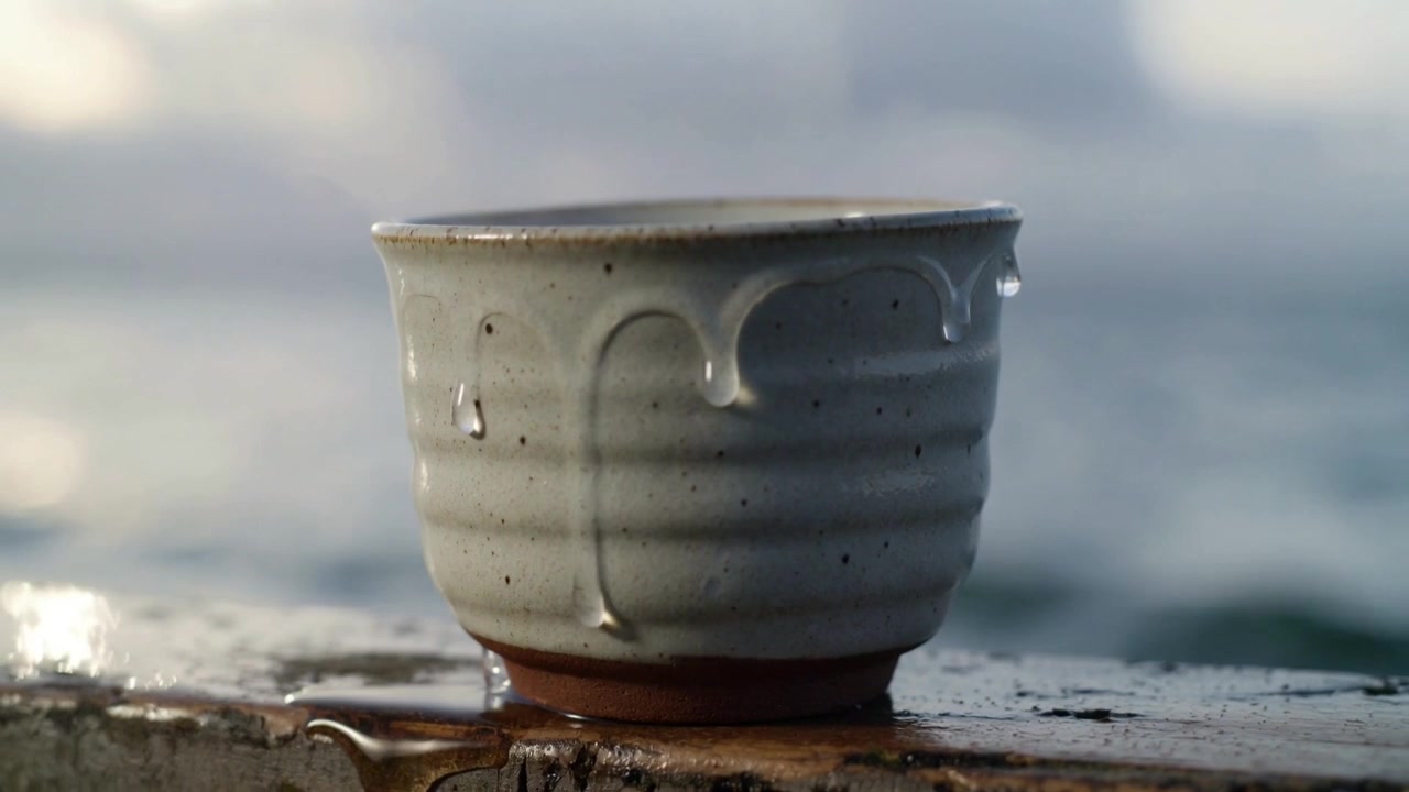 Gocciolante dal bordo bagnato, piccola tazza di ceramica che rilascia rivoli e goccioline su una sporgenza consumata dal mare