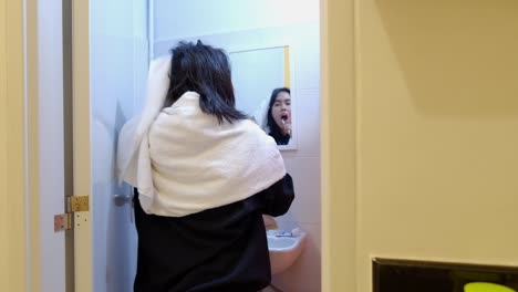 una mujer joven se cepilla los dientes frente al espejo en el baño después de la ducha