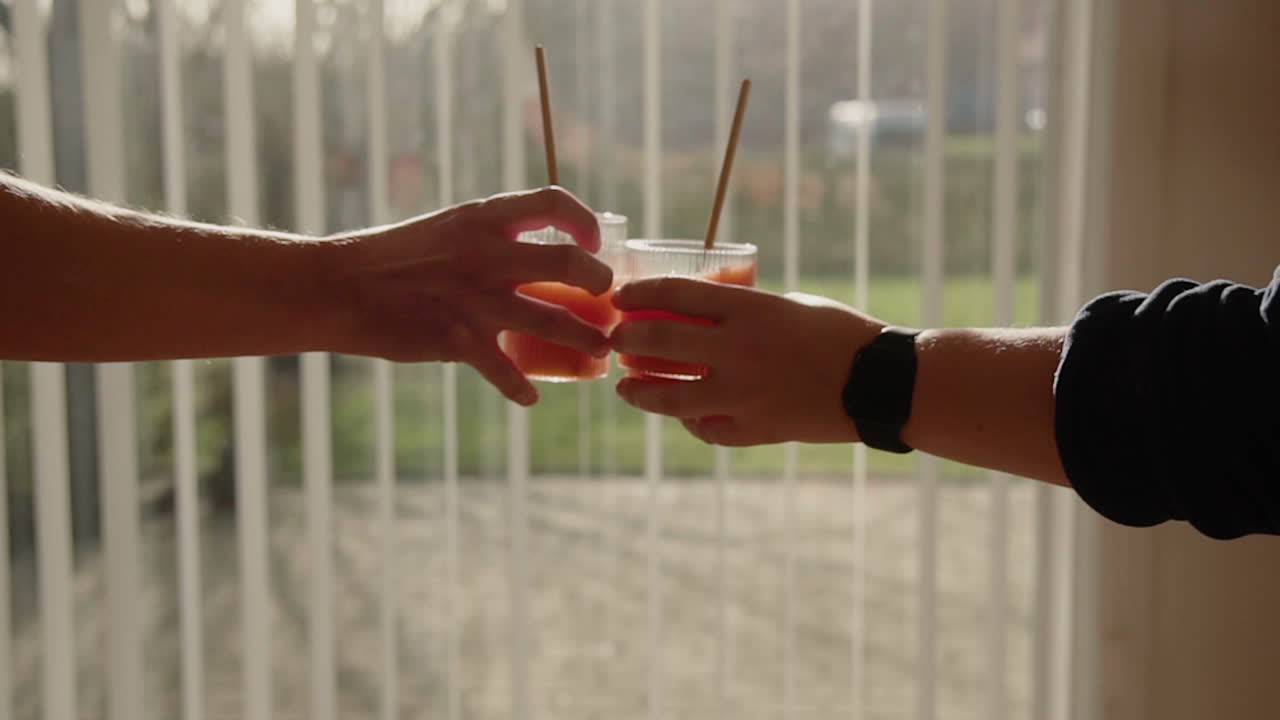 A man and a woman cheering with Orange Cold Pressed Juice in two drinking glasses with metal straws in slow motion Detox Cleanse