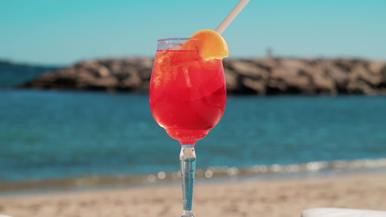 Un cocktail rinfrescante rosso-arancio con ghiaccio e fetta d'arancia sullo sfondo del blu intenso del Mar Mediterraneo