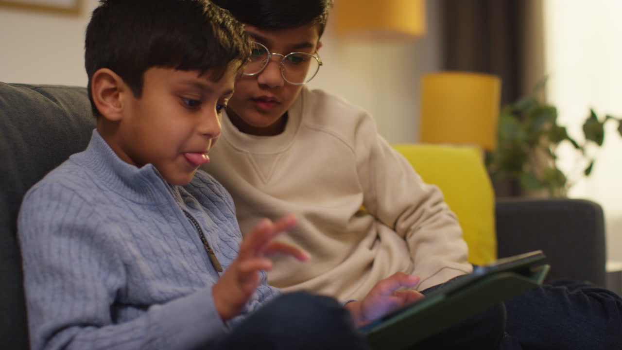 Two Young Boys Sitting On Sofa At Home Playing Games Or Streaming Onto Digital Tablet 1
