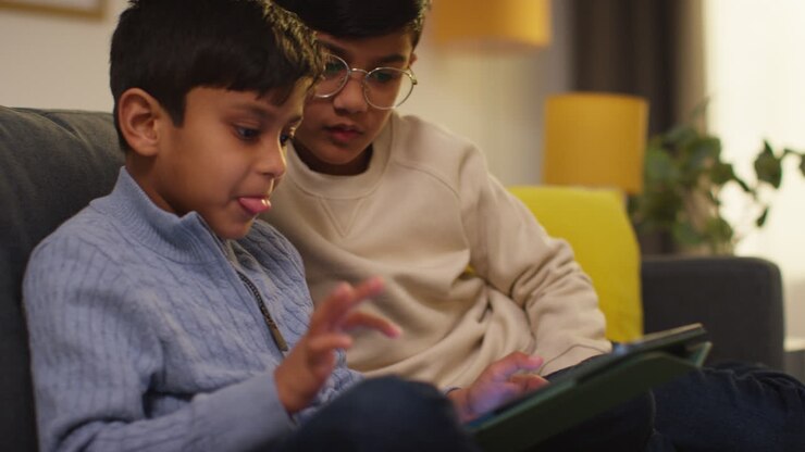 Zwei junge Jungen sitzen zu Hause auf dem Sofa, spielen Spiele oder streamen auf einem digitalen Tablet 1