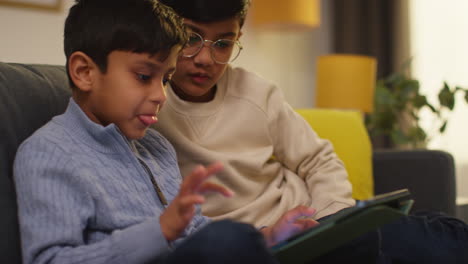 two young boys sitting on sofa at home playing games or streaming onto digital tablet 1