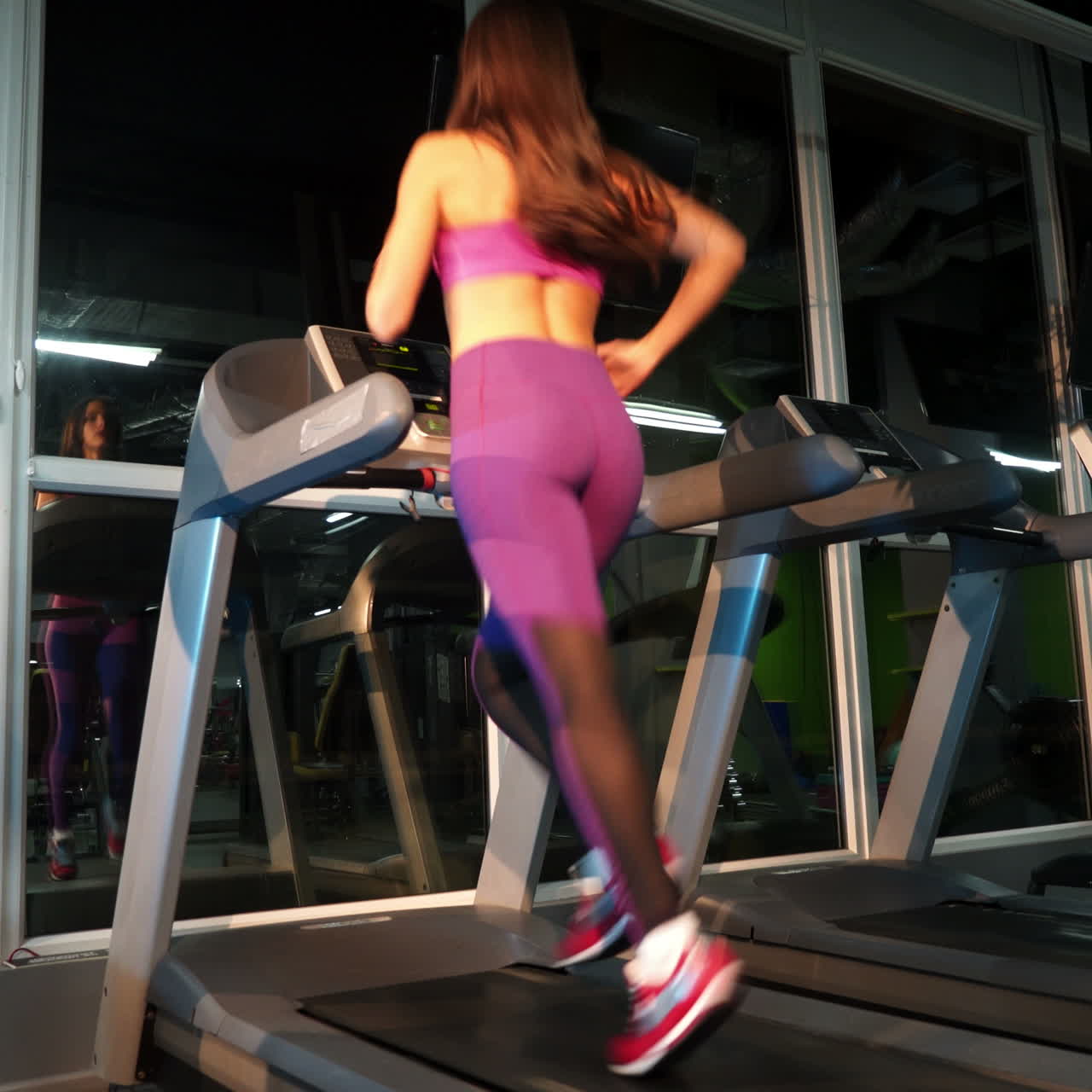 Back view of a brunette woman running on a racetrack while working out in a sport club. Active female training on a modern simulator in a new center