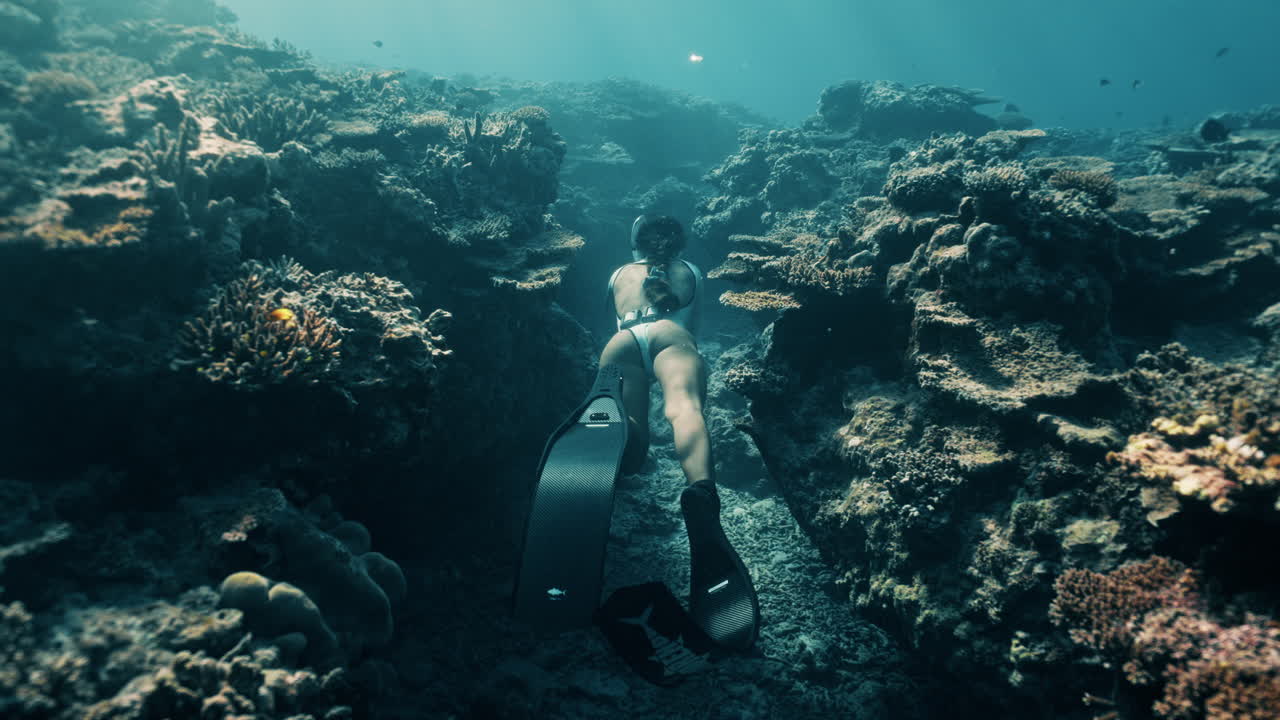 Underwater shot of a freediver moving past coral formations in the deep blue, showcasing strength, grace, and connection to the marine world