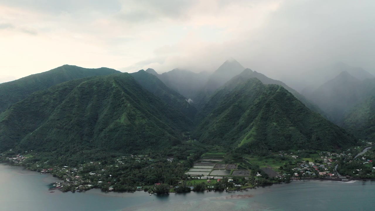Teahupoo, Tahiti üzerinde geniş açılı havadan çekim, nehir aşağıda kıyıdaki küçük bir köye doğru kıvrılırken dik yağmur ormanı sırtlarına tutunan sürüklenen sis