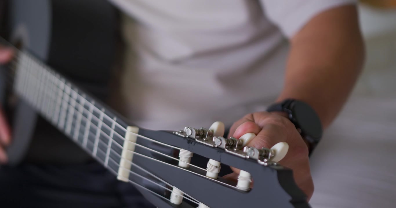 Right hand is turning white tuning peg after hearing low string pitch, tuning guitar on couch