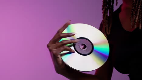 a person's hand holding and interacting with a reflective cd or dvd against a purple background