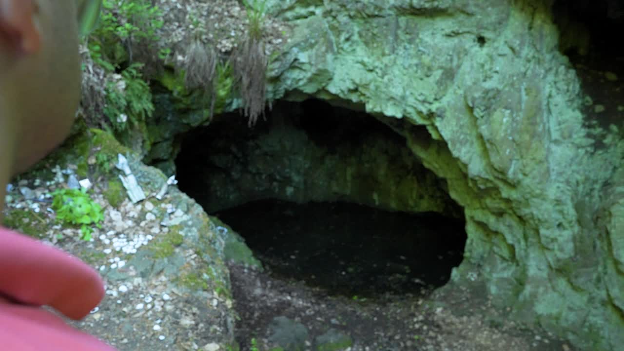 pasando por el turista de pie frente a la entrada de la abertura de la cueva, conocida como la ubicación del santuario de la diosa guerrera egipcia bastet en la montaña strandzha en bulgaria