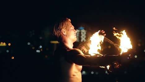 young blond male spins two burning pois tied together slow motion shot close-up shot