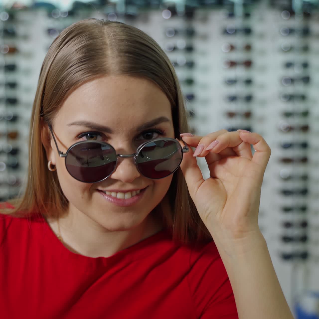 Beautiful woman trying on stylish sunglasses. Long-haired girl in modern black sunglasses posing on camera at optical store.