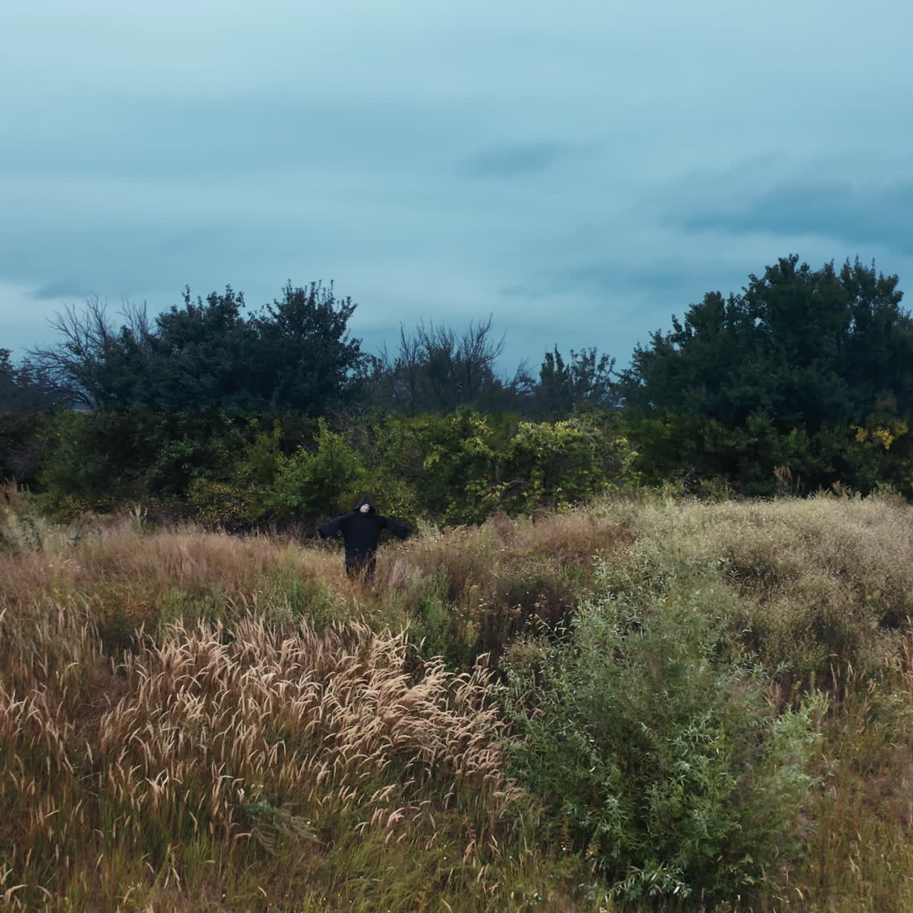 Dark ghost with outstretched arms. Scary figure of death in black mantle with hood standing on the field. Motion camera back. Halloween concept.