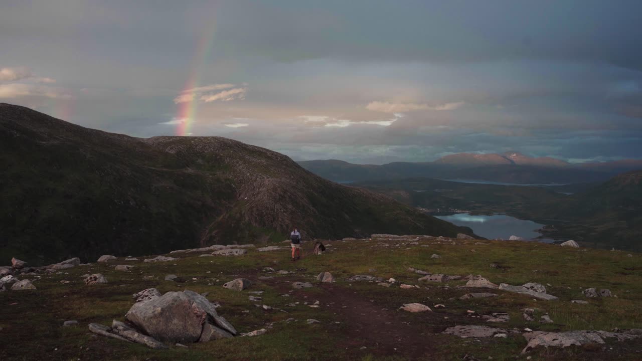 viajera y perro mascota haciendo senderismo en grytetippen en noruega con vista al arco iris en el cielo al atardecer
