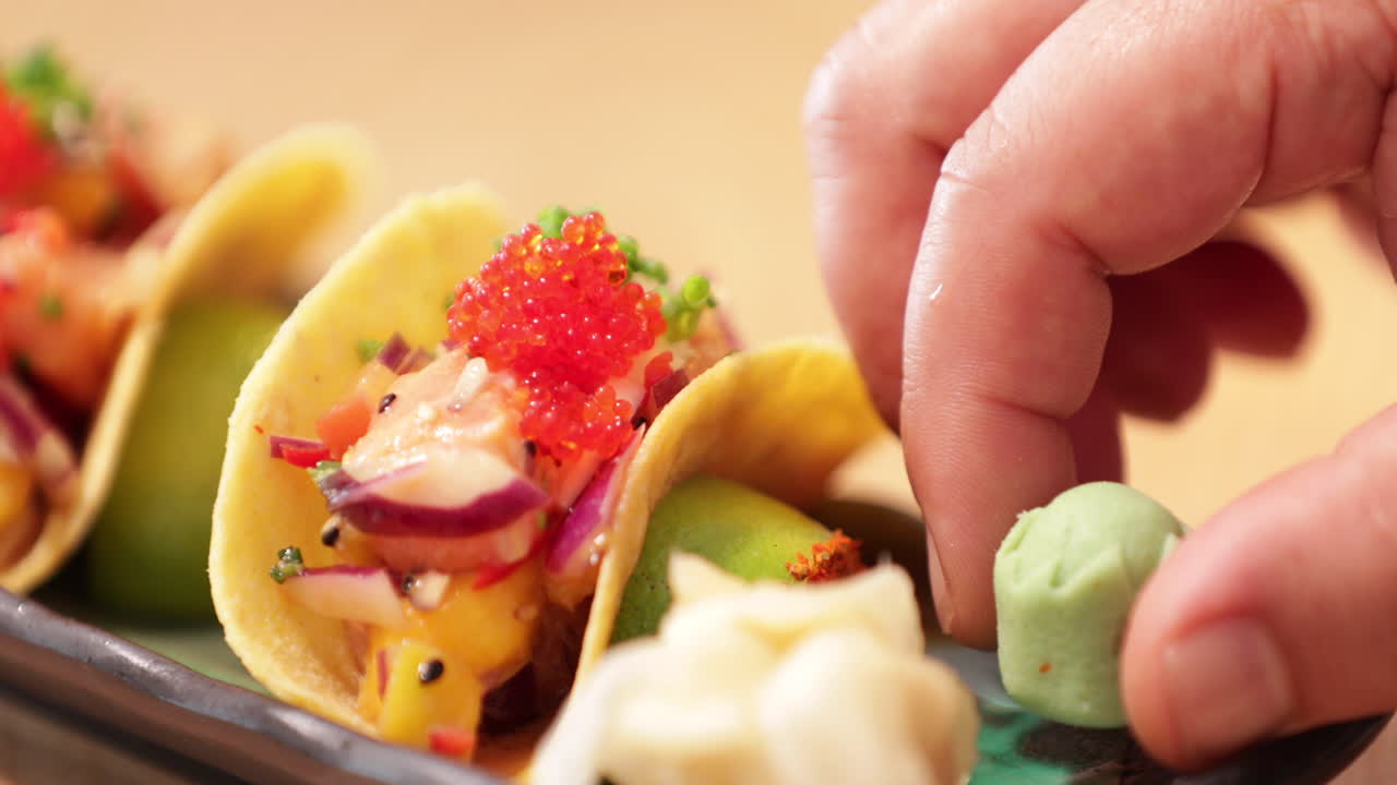 셰프가 서빙하기 전에 스시 타코 옆에 와사비를 얹고 있습니다