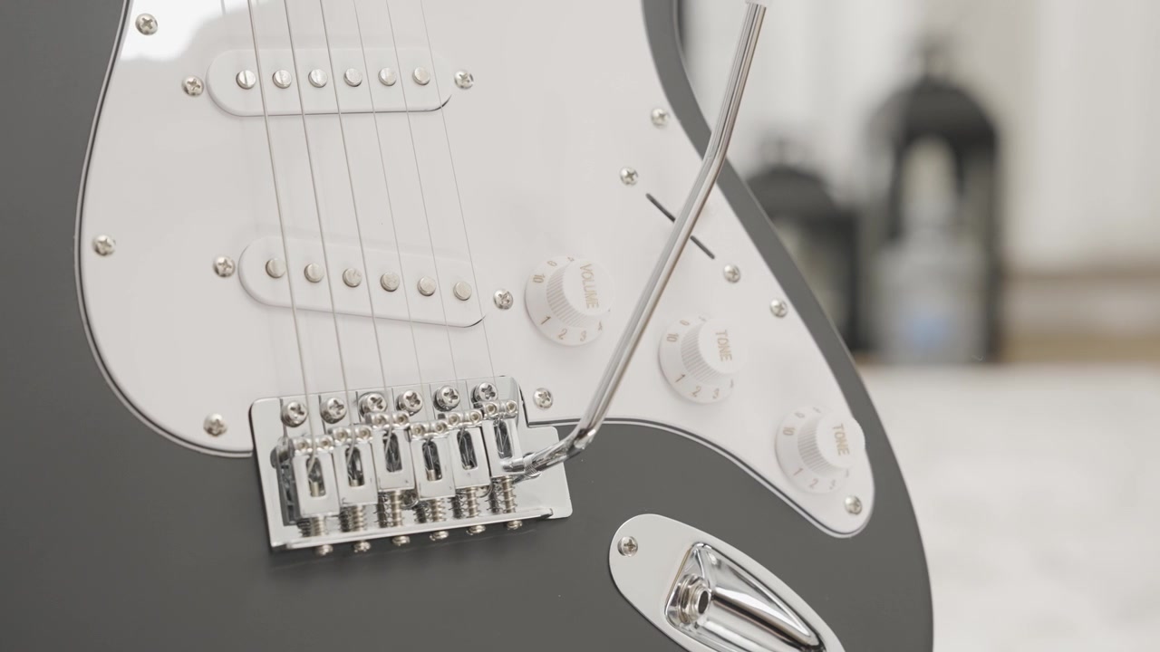 Nærbillede af en sort Stratocaster-stil elguitar i en stue.