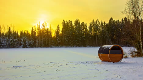 Sauna-De-Barril-En-Campo-Nevado-Con-Bosque-De-Coníferas-En-El-Fondo-Y-Cielo-De-Puesta-De-Sol-Amarillo-Brillante