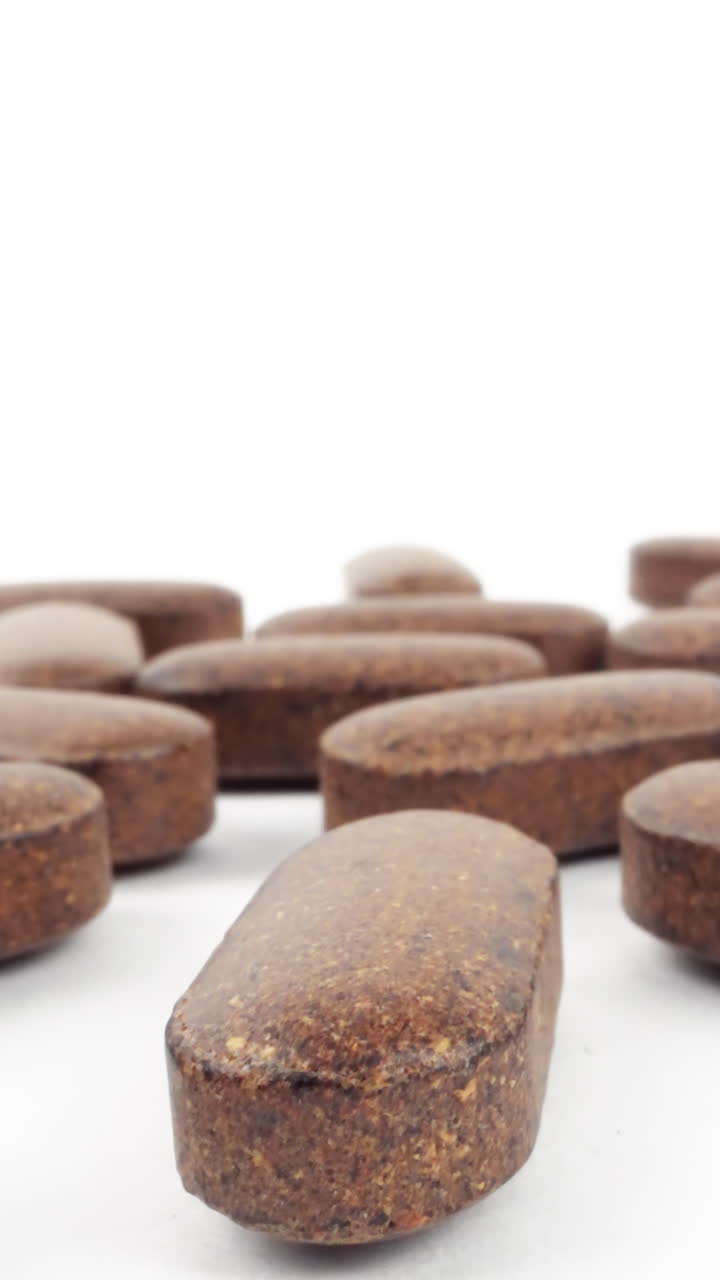 primer plano de varias pastillas de suplementos herbales esparcidas sobre un fondo blanco
