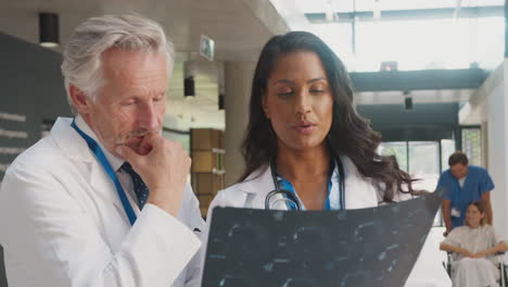 Close-Up-Of-Doctor-Wearing-White-Coat-Discussing-Patient-Scan-With-Female-Colleague-In-Hospital