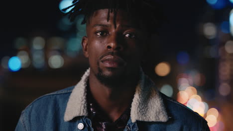 portrait of attractive young african american man on rooftop at night wearing stylish fashion with bokeh city lights in urban skyline background