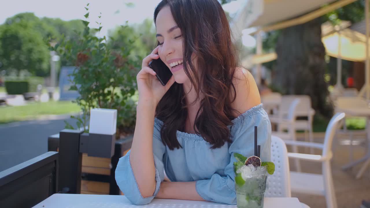 야외 레스토랑에 앉아 휴대전화로 통화하는 예쁜 브루네트 여성