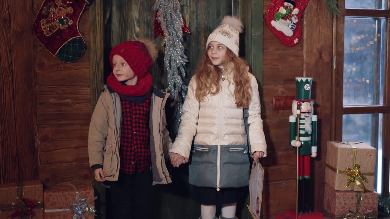 Little boy and girl with envelope coming into Santas residence. Children looking wonderingly inside the decorated house at Christmas.