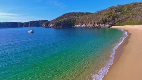 vista estacionaria en ángulo bajo de la cala de la playa de aguas tranquilas con un velero anclado distante