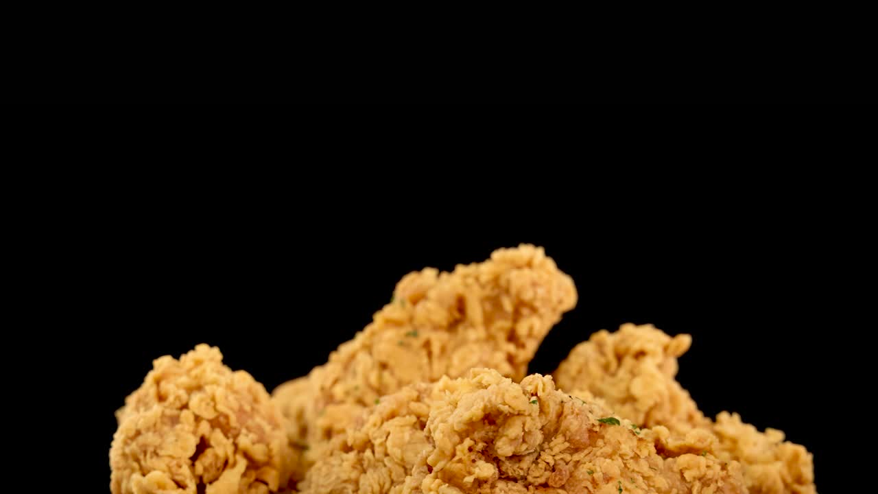 Golden, crispy fried chicken breasts and thighs rotate in slow motion against a black background, highlighting crunchy texture and even lighting with copy space