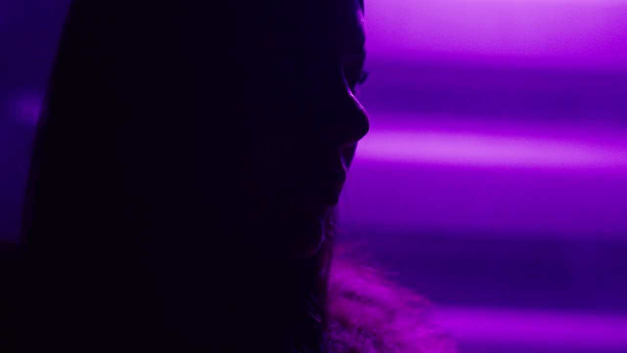 Silhouette ravvicinata di una donna circondata da nebbia viola e luci al neon, che crea un'atmosfera misteriosa, artistica e cinematografica