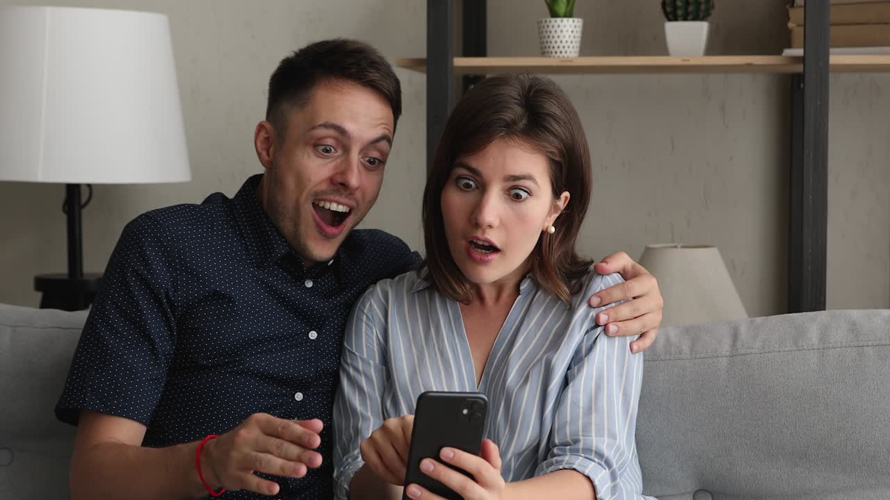 una pareja mirando un teléfono inteligente celebra la victoria en un juego de apuestas en línea.