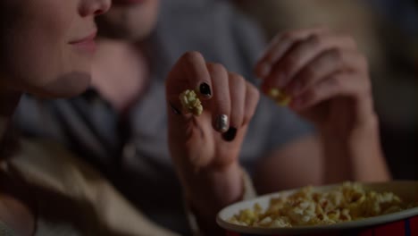 female and male hands take popcorn from paper bucket. eating pop corn at cinema