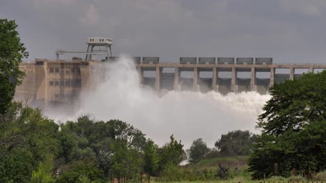 downstream view of power dam releasing torrent of turbid flood water