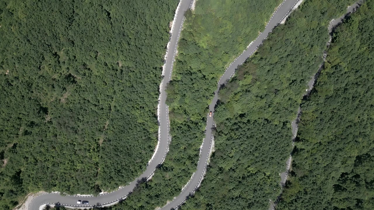 Pemandangan udara dari atas tikungan tajam berbentuk jepit rambut di jalan pegunungan yang berkelok-kelok dikelilingi hutan hijau lebat di Transalpina de Apuseni.