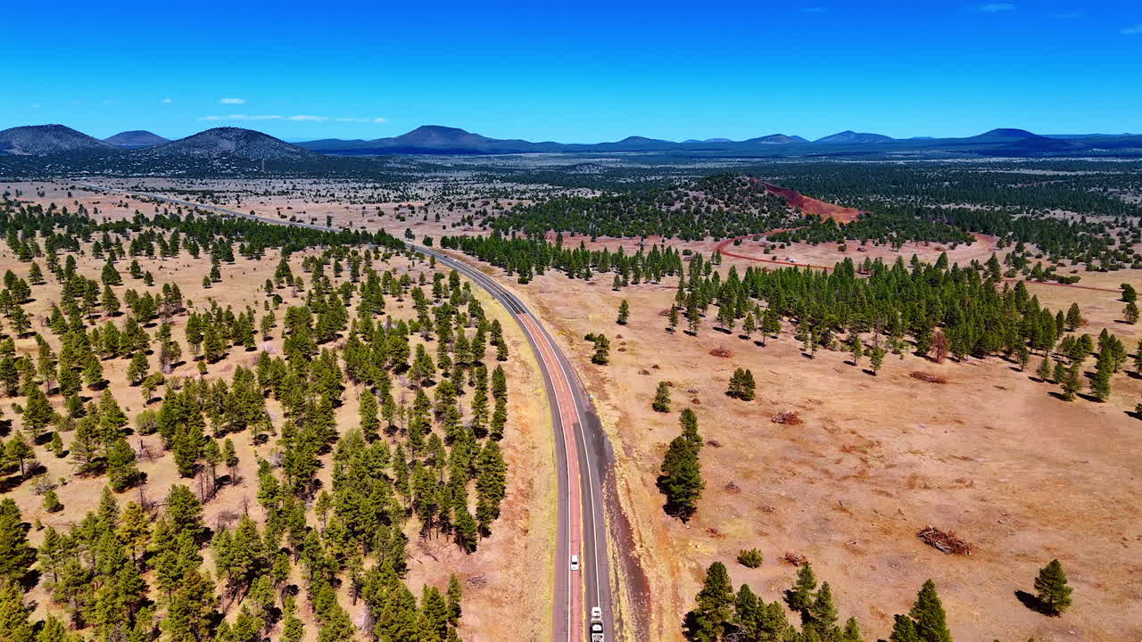 Two-lane road in the deserted lands covered with scarce pine tree woods. Silhouette of mountain range at backdrop. Arizona, USA