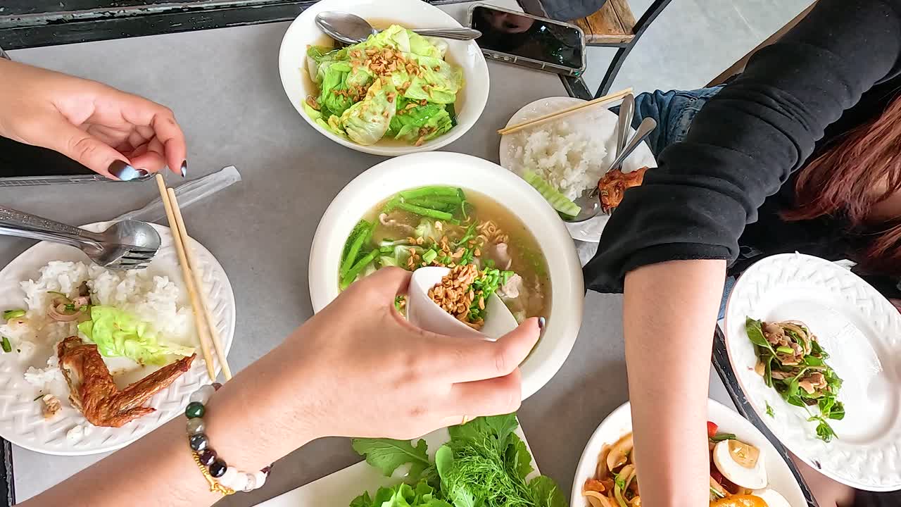 Hands preparing and enjoying traditional Lao dishes in a vibrant setting. Bright lighting enhances the colorful and inviting atmosphere