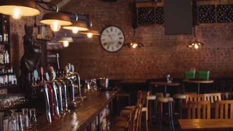 interior de un bar o pub vacío, con grifos de cerveza, mesas y sillas de madera y pared de ladrillo expuesta