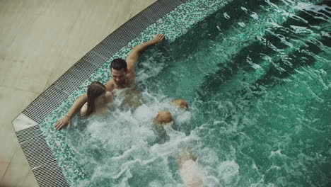 Familia-Feliz-Descansando-En-La-Piscina-Spa-Cubierta.-Pareja-Joven,-Relajante,-En,-Bañera-De-Hidromasaje