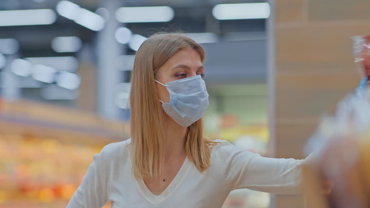 retrato, una mujer joven con una máscara médica toma pan de un estante de supermercado. mujer está haciendo compras en la sección de pan del supermercato. movimiento circular de la cámara. 4k, prores