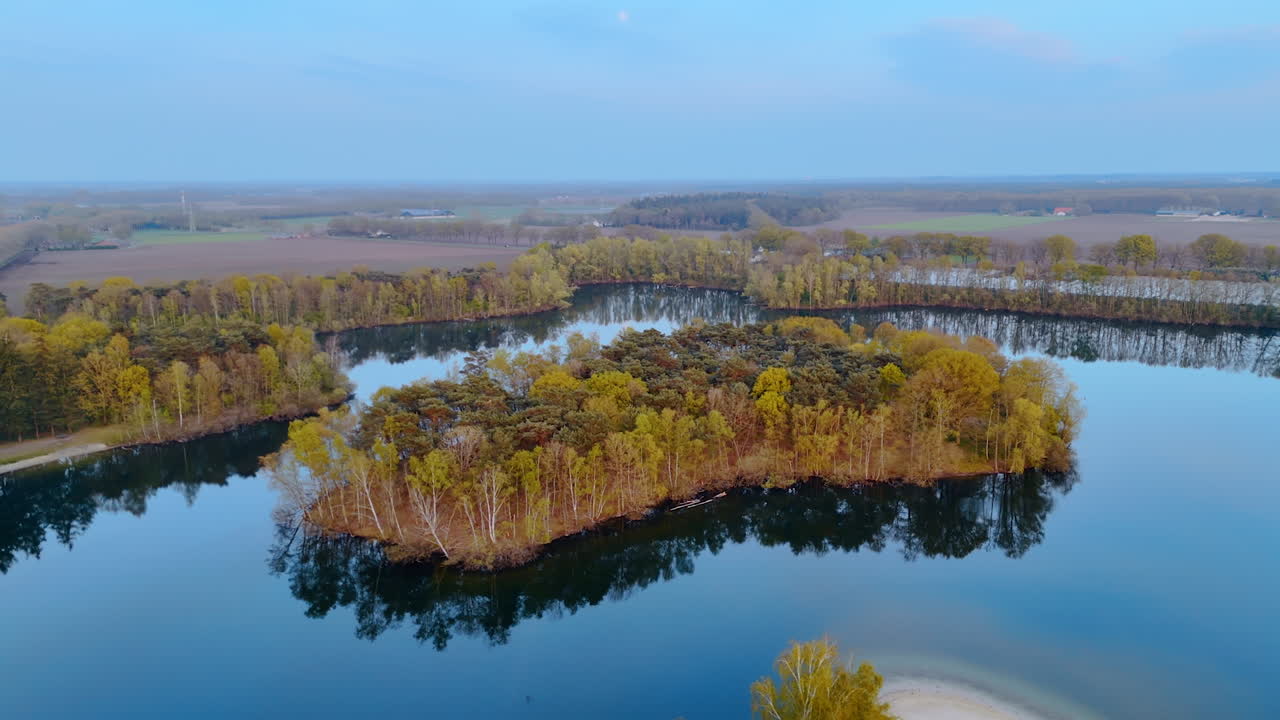 Green island in water, Netherlands. Aerial view showcases a serene green island in a calm body of water with distant fields in the background at twilight