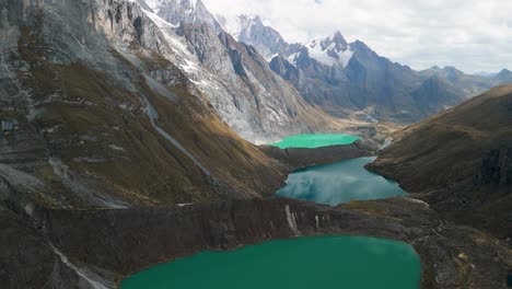 a breathtaking aerial shot tilts up from the three turquoise glacial lakes (tres lagunas) to reveal the majestic, snow-capped mountain peaks of the huayhuash trek in peru