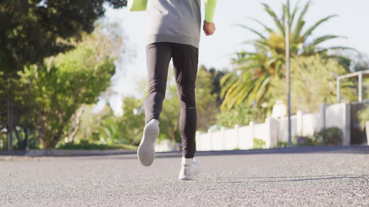 video de la vista trasera de un hombre de dos razas en ropa deportiva corriendo en una calle soleada