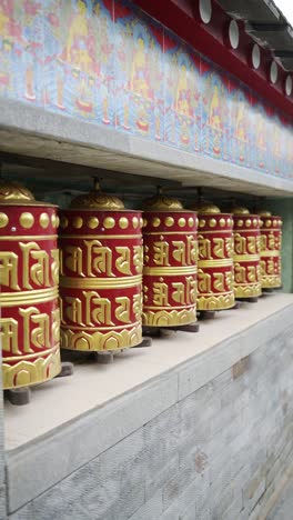 vertical tibetan prayer wheels in nepal, close up detail of beautiful decoration of red and gold leaf prayer wheels at a buddhist temple, vertical video for social media instagram reels and tiktok